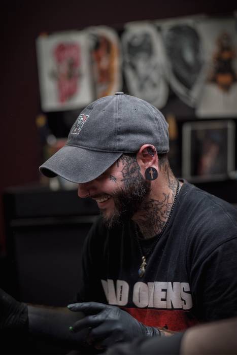 Justin Styndl working at Cardinal Ink, wearing a cap and tattoo gloves